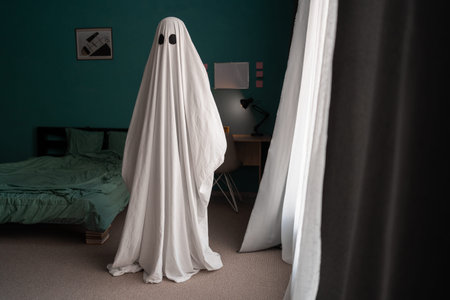 Ghost covered with a white ghost sheet on a bedroom in new house. Halloween