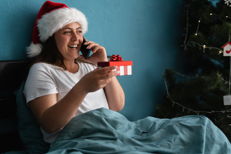 Happy young woman talking on the phone and holding gift at home at Christmas.の写真素材