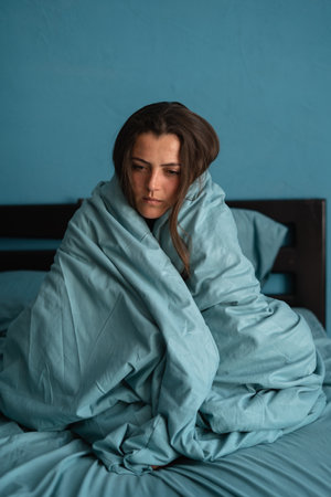 Sad female, worried, suffers from insomnia and headache. Girl sits on bed in bedroom. Migraines, health and mental problems. Lack of sleep and depression concept.の写真素材