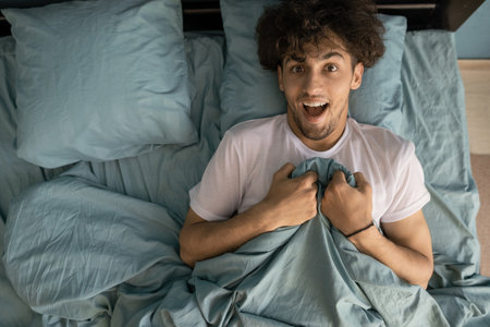 Top view of a young man lying in bed in the morning covered with a blanketの写真素材