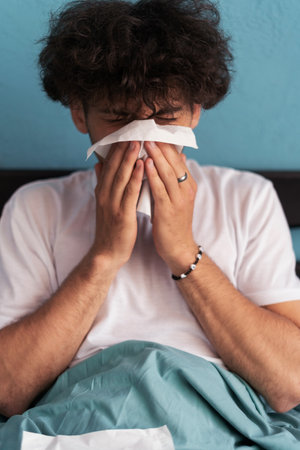 Cold and flu concept. Sick man suffering from running stuffy nose. Upset ill guy blowing her nose using paper napkin tissueの写真素材