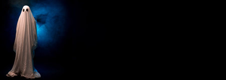 Scary ghost on a dark background in the fog. An evil spirit covered in sheet.
