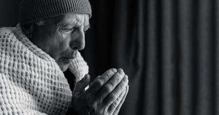 Senior man freezing at home, standing near window and heating his hands. Old man with home heating problem feeling cold. Black and white photoの写真素材