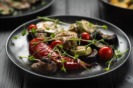 Close-up view of grilled vegetables, tomato, zucchini paprika on plate over black backgroundの写真素材