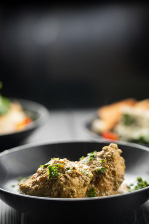 Chicken breast in creamy garlic sauce in plate on lack background with other dishes