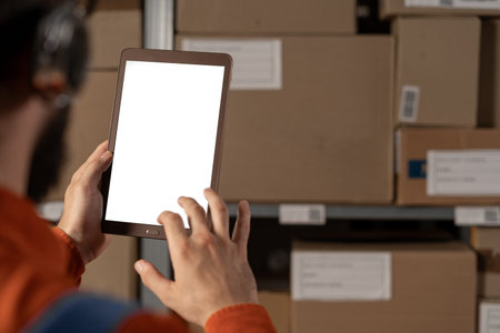 male worker uses digital tablet with blank screen in the retail warehouse full of shelves with...