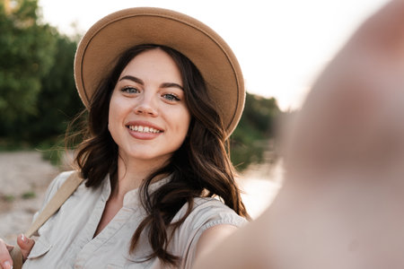 Young woman taking selfie portrait outside. Smiling happy girl wearing hat enjoying summer holidays at the beachの写真素材