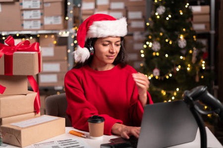 Santa claus working in christmas office at night, sitting at laptop takes customer order for delivery of gift box, entrepreneur small business owner in store warehouse, SME, christmas saleの写真素材