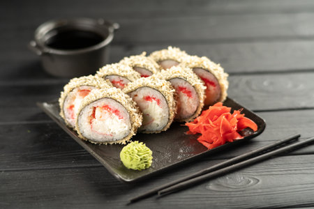 Fried hot sushi roll with shrimp, smoked eel, cream cheese with chopsticks and sauce on black background. Sushi menu. Japanese food concept.の写真素材