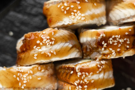 Close-up sushi roll with cream cheese and eel on stone dark plate on black wooden background. Japanese food. Teriyaki sauceの写真素材