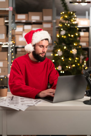 Happy Santa Claus wearing hat using laptop computer sitting at workshop table on Christmas. Ecommerce website, online shopping sale concept.の写真素材