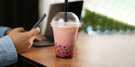 Male hands with mobile phone and bubble ice milk tea served in takeaway glass on the tableの写真素材