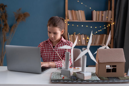 Little girl with laptop computer and wind turbines model at home making paper project for school. Renewable energy, children, technology, science and peopleの写真素材