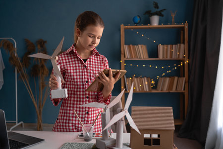 Elementary school, girl holding tablet computer studying how wind turbines work working at home with project. Children learning about eco-friendly forms of renewable energyの写真素材
