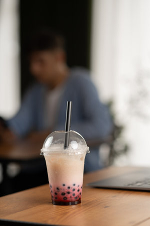 Plastic cup of fresh bubble drinks on wooden table in cafe over male client backgroundの写真素材