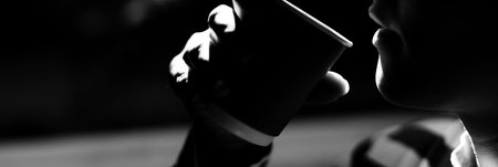 Black and white side view dramatic light shot of young woman holding paper cup with espresso on black background.の写真素材