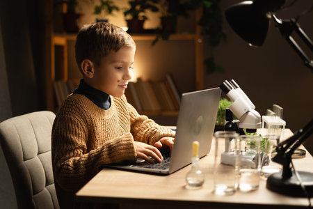 Child using laptop and microscope in the evening at home. Science education