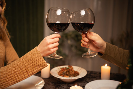 Romantic dinner concept. Celebrating Valentines Day. Couples hands clinking glasses of red wine dating in restaurantの写真素材