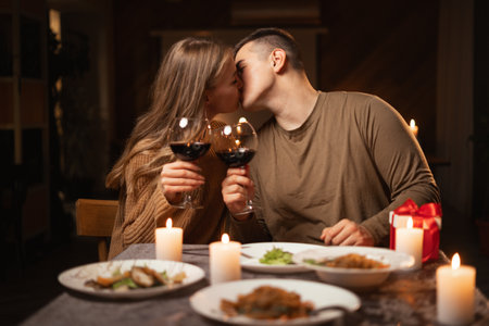 Happy young couple in love kissing, having romantic dinner celebrating Valentines day, drinking red wine at home or in restaurant.の写真素材