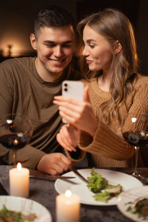 Happy young couple using smartphone browsing internet during romantic date dinner at home.の写真素材