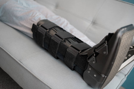 Close-up of ankle sprain orthosis, black splint on leg on sofa at home.