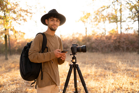 Travel photographer with mobile phone taking a photo with nature in sunset at autumn with camera on tripod. Natural photography relaxingの写真素材