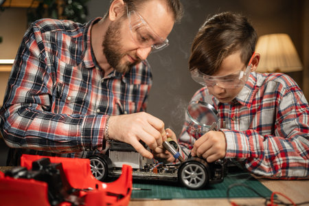 Father teaching his son for soldering and repair remote controlled car at home. Man and boy fixing...