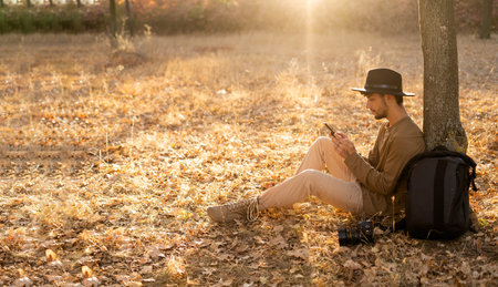 Photographer resting in an autumn park under a tree using a smartphone for freelancingの写真素材