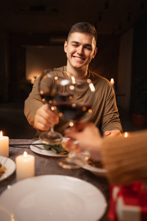 Cheerful happy couple in love drinking wine and having romantic dinner at home or restaurant. Home date and clinking wine glasses.の写真素材