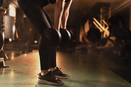Fitness woman in tight sportswear is training in the gym. exercise with dumbbells deadlift, back...