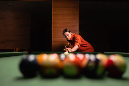 A woman playing billiards at a billiard table, preparing to break a pyramid of multi-colored balls,...