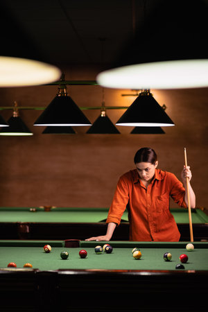 Beautiful woman looking at billiard balls on table trying to hit the ballの写真素材