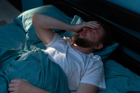 Depressed millennial tired man awake in the night touching his forehead and suffering from insomniaの写真素材