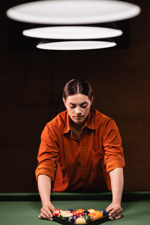 Young brazilian woman placing colorful pyramid of billiard balls in billiard triangle on green pool table.の写真素材