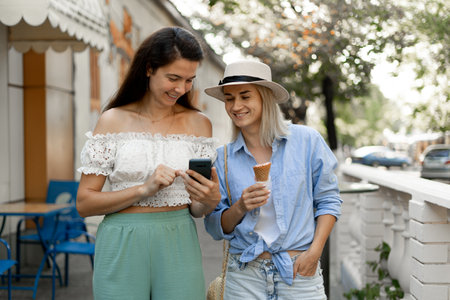 Holidays, travel, friends and tourism concept. Two friends walking in old town and looking photos on smartphone.の写真素材
