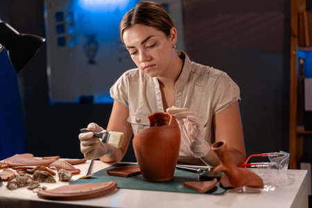 Archaeologist cleaning antique vessel with brush working late night in the office