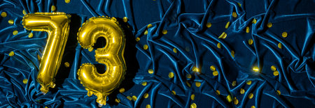 Gold foil balloon number number 73 on a background of blue velvet decoration. Birthday greeting...