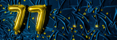 Gold foil balloon number number 77 on a background of blue velvet decoration. Birthday greeting...