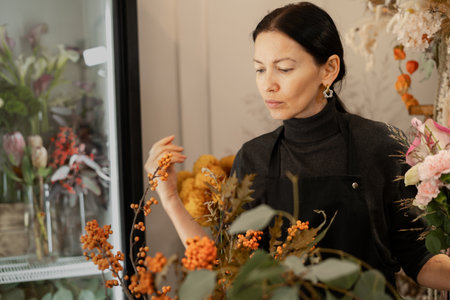 Hispanic florist arranging a bouquet of beautiful colorful autumnal flowers working in her floral shopの写真素材