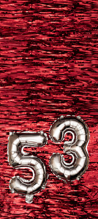 Silver foil balloon number number 53 on a background of red tinsel decoration. Birthday greeting...