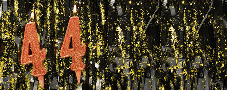 Burning red birthday candles on glitter tinsel background, number 44. Banner.の写真素材
