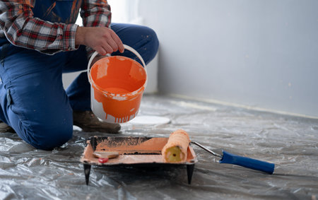 Close-up of male hands pouring paint into the tray. Professional interior painter worker pouring orange color paint to tray.の写真素材