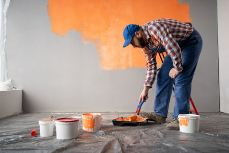 Concentrated handyman in overalls is preparing paint roller for workの写真素材