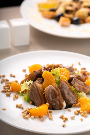 Salad with duck breast, tangerines, oranges and pine nuts served on a white plate in a restaurant on the table.の写真素材