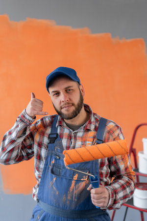 Bearded man holding roller painter smiling doing phone gesture with fingers like talking on the phone. communication concept.の写真素材