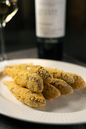 Mullet fish fried in breadcrumbs served on a white plate with wine in the background. Restaurant menu concept.の写真素材