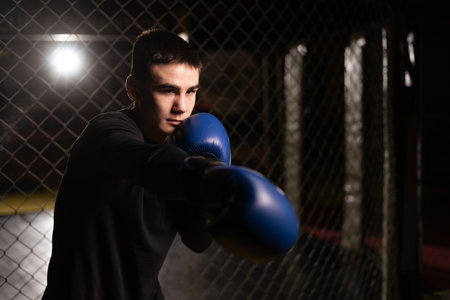 Boxer practicing his punches at a boxing studio. Young man punching inside a boxing cage, close-up.の写真素材