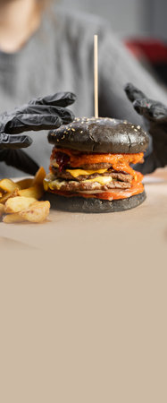 Fast food, people and unhealthy eating concept. woman hands in gloves holding black hamburger or burger sitting in restaurant. Copy spaceの写真素材