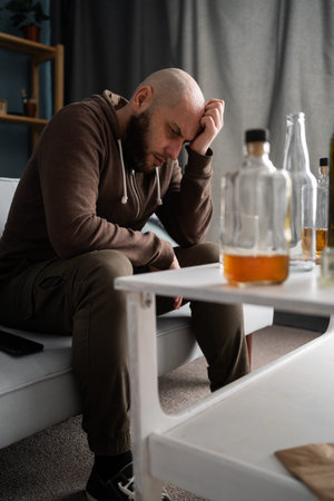 Lonely depressed man drinking whisky and suffering headache at home
