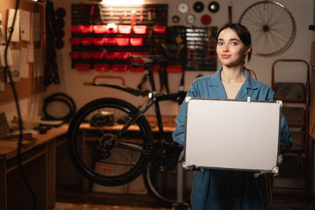 Young handywoman showing empty board for advertising standing in the workshop or garage. Concept of...